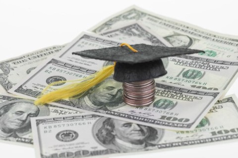 Stack of coins with a graduation cap on top, surrounded by 100-dollar bills.
