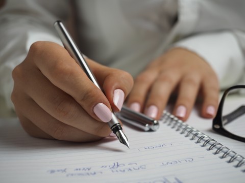 a closeup of hands writing on a notebook