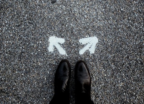 Feet standing on pavement with two arrows pointing in opposite directions to symbolize choosing a path.
