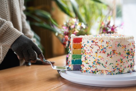 A person wearing compression gloves removes a slice of rainbow cake