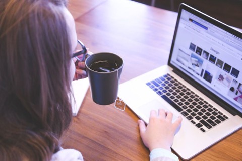 Image of a person typing on a laptop and holding a coffee mug