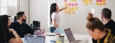 woman looking at Post-it notes on a wall while colleagues look on