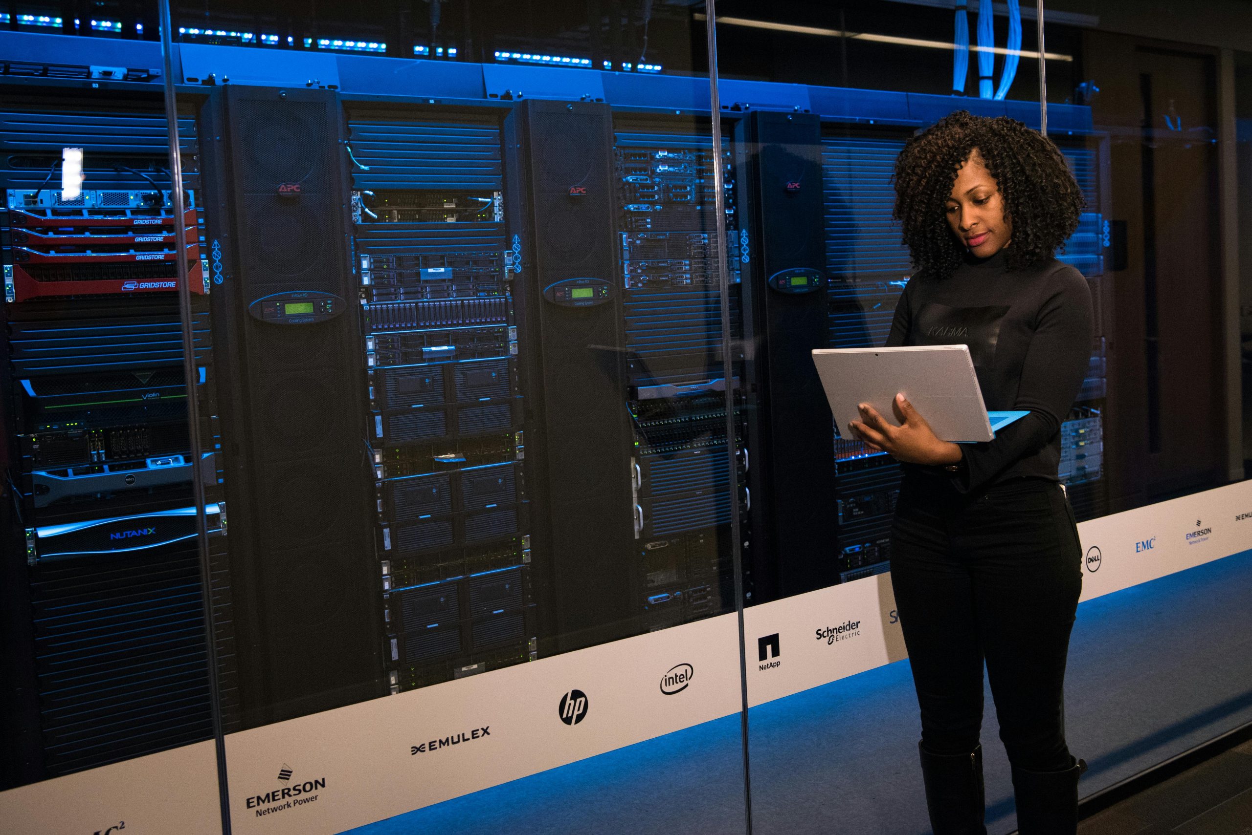A woman is standing next to a wall of system hard drives.