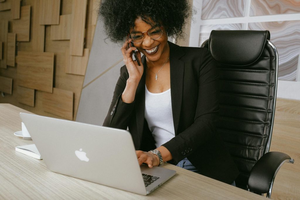 Woman sitting at laptop, smiling, while on the phone.