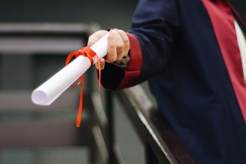 Hand holding out a diploma, wrapped in red ribbon.