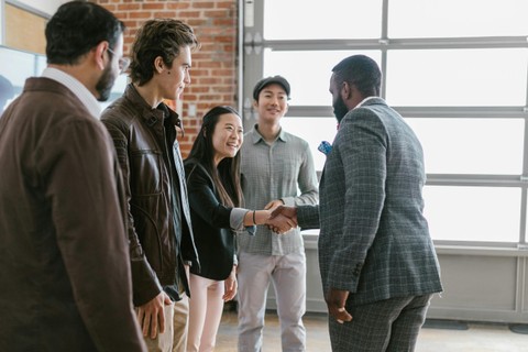 Black man in suit meeting and shaking hands with group of fellow professionals