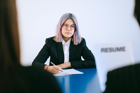 Woman interviewing in dark suit jacket with pastel-dyed hair. Interviewer with resume in foreground