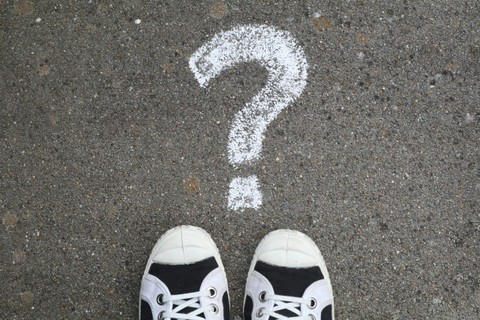 White chalk question mark on the ground with the toes of shoes visible just below