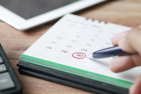 Paper calendar on a desk with the 30th circled in red and a hand holding a pen