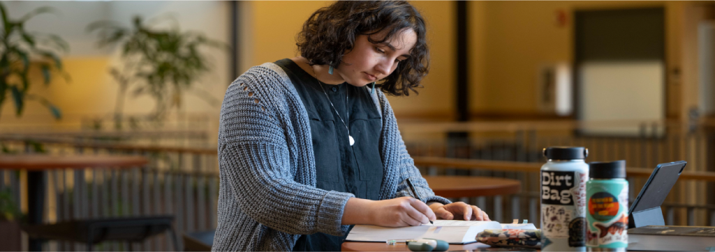 Student standing at a table, highlighting or making a note in a text book