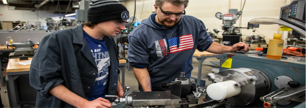 Techer showing a student how to use a large piece of machinery
