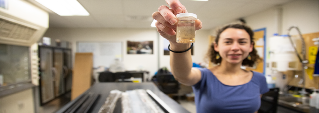 a female student smiling at the camera holding up a specimen cup