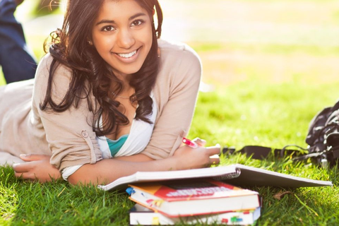 Smiling young woman lying in the grass with books