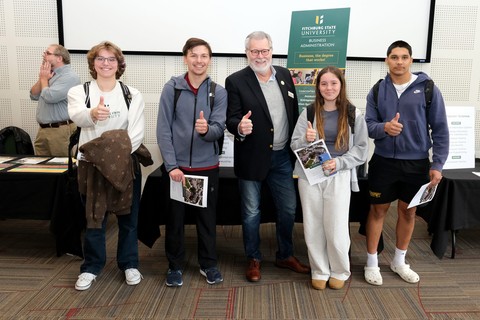 four students and one faculty member smiling holding thumbs up