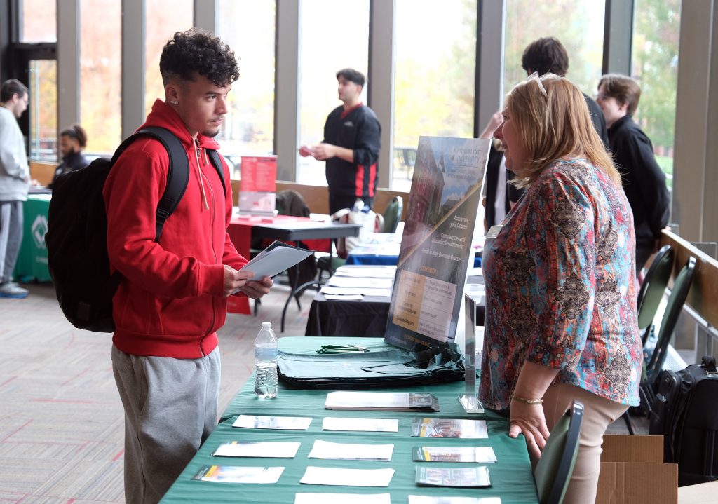 Student with a backpack speaks with a woman behind an information table at a career fair