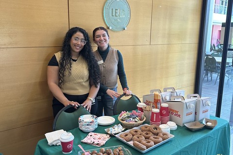 Two career advisors stand behind a table full of pumpkin spice doughnuts and coffee