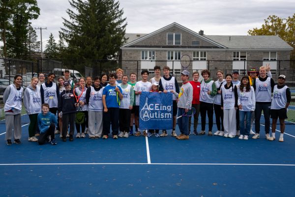 Group of students and athletes wearing ACEing Autism jerserys stand on a tennis court and pose for a photo.