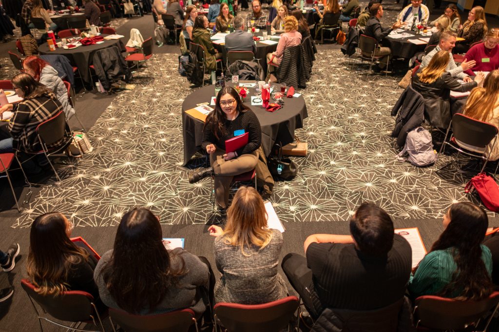 A group of students attend a conference in a large room.