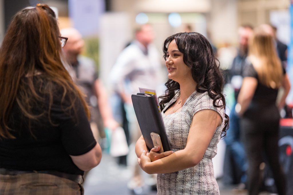 A student holding a binder speaks with a company representative at a job fair.