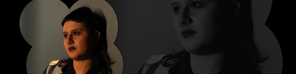 A non-binary person wearing a button down and an edgy wolf cut looks up thoughtfully towards a warm light