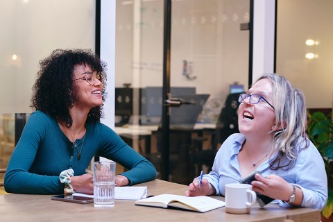 UK, London, Two smiling women writing in notebooks in modern office