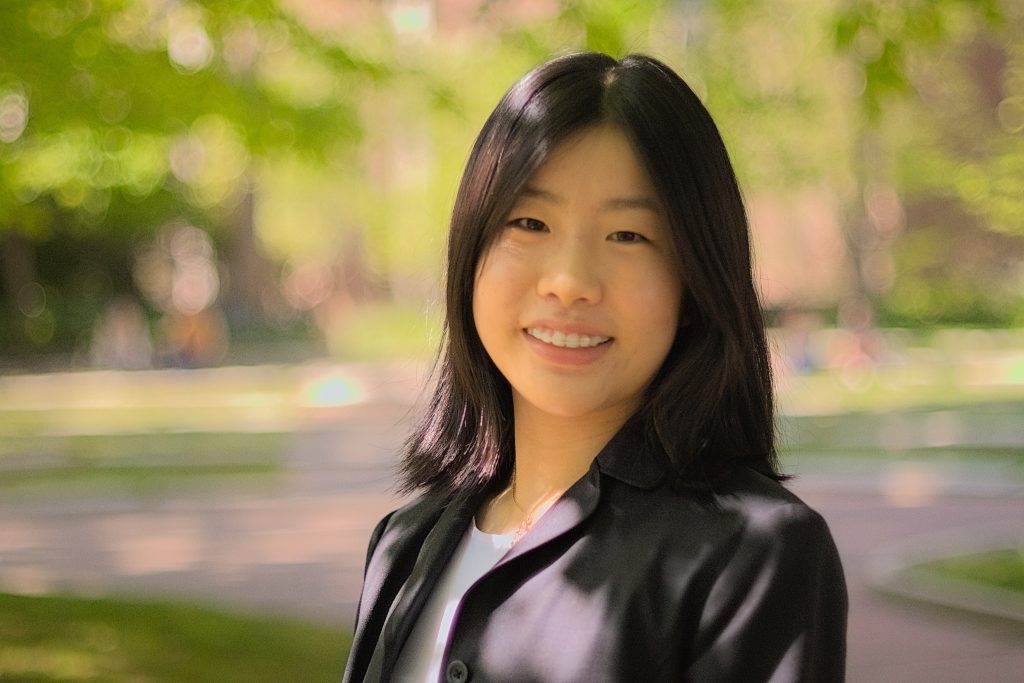 Rachel smiling in a black blazer in front of out-of-focus trees
