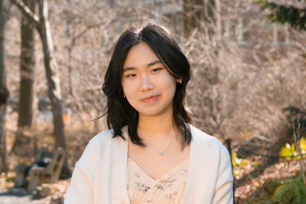 Emily smiling in an off-white shirt in the woods
