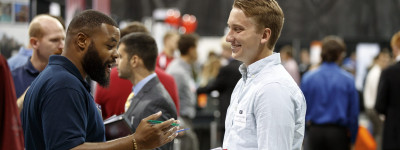 Pictured here: A student and employer talking and smiling at a career fair.
