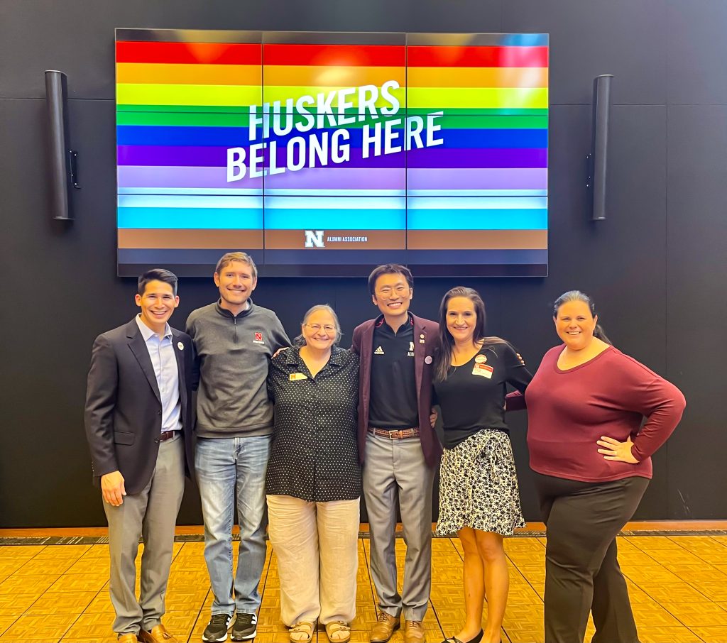 Pride in the Workplace planning team members standing in front of rainbow colored event sign.