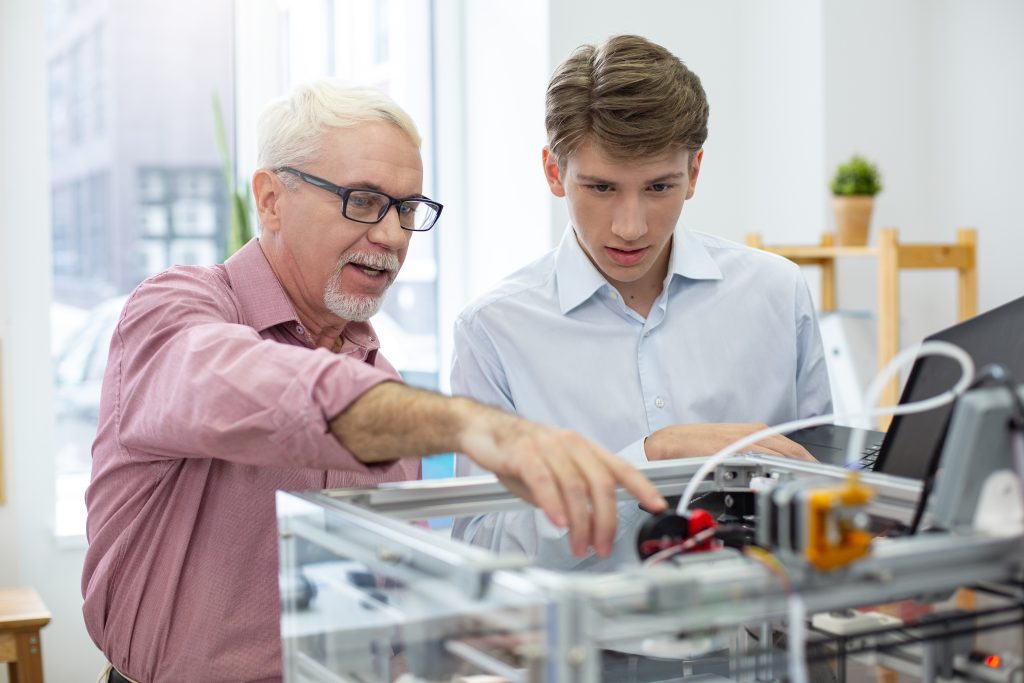 Older male professional showing a younger male student how a machine works.